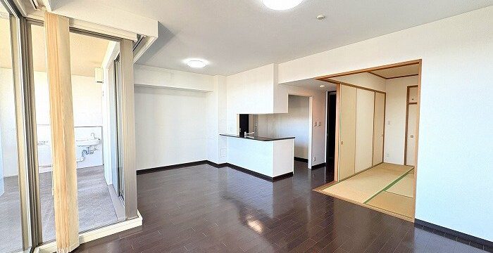 Open-concept living space with dark wood floors, white walls, a kitchen island, and a tatami-room doorway on the right; glass balcony doors on the left.