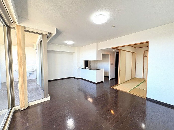 Open-concept living space with dark wood floors, white walls, a kitchen island, and a tatami-room doorway on the right; glass balcony doors on the left.