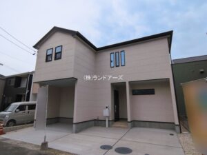 海部郡第2大治町長牧中道_3号棟_20260318_1_0863592 - 株式会社ランドアーズ|名古屋の一戸建て(建売・中古戸建)・中古マンション・賃貸管理・不動産売却 Front view of a beige, two-story modern house with an angular roof and a paved driveway; a silver van is parked to the left, with Japanese text on the facade.