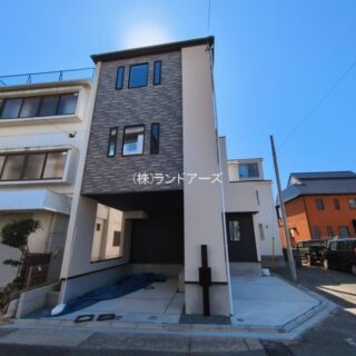 Narrow, modern three-story house with a dark brick facade on a residential street under a clear blue sky.