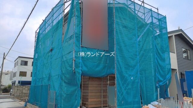 House under construction wrapped in blue construction netting with scaffolding along a residential street.