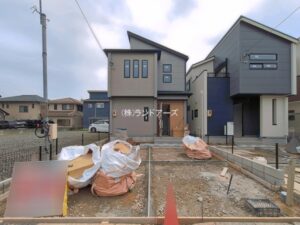 Construction site in front of two modern suburban houses; piles of wrapped construction debris on dirt lot and a traffic cone in the foreground.