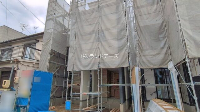Under-construction house with metal scaffolding and gray protective netting surrounding the façade.