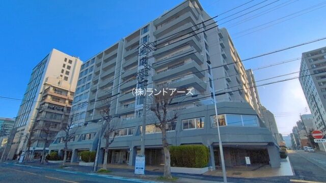 Six-story apartment building on a city street with bare trees and power lines; façade shows (株)ランドアーズ.