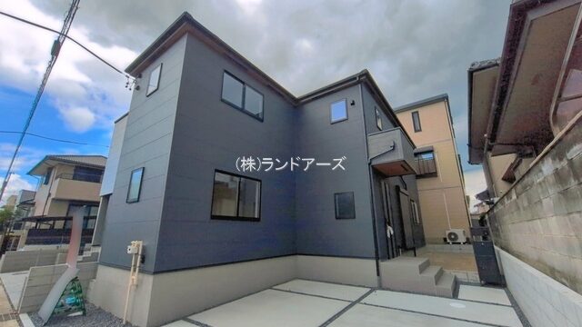 Modern gray two‑story house with angular lines, a concrete driveway, and neighboring homes under a cloudy sky.