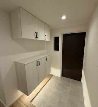 Entryway with two-tone gray wall cabinets (upper and lower), a light wood base, and a dark front door.