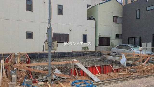 Construction site with wooden formwork and rebar for a building foundation in a city block.