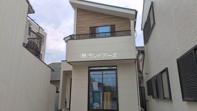 Two-story beige house with a wooden accent and balcony, front window, at a construction site with materials on the left.